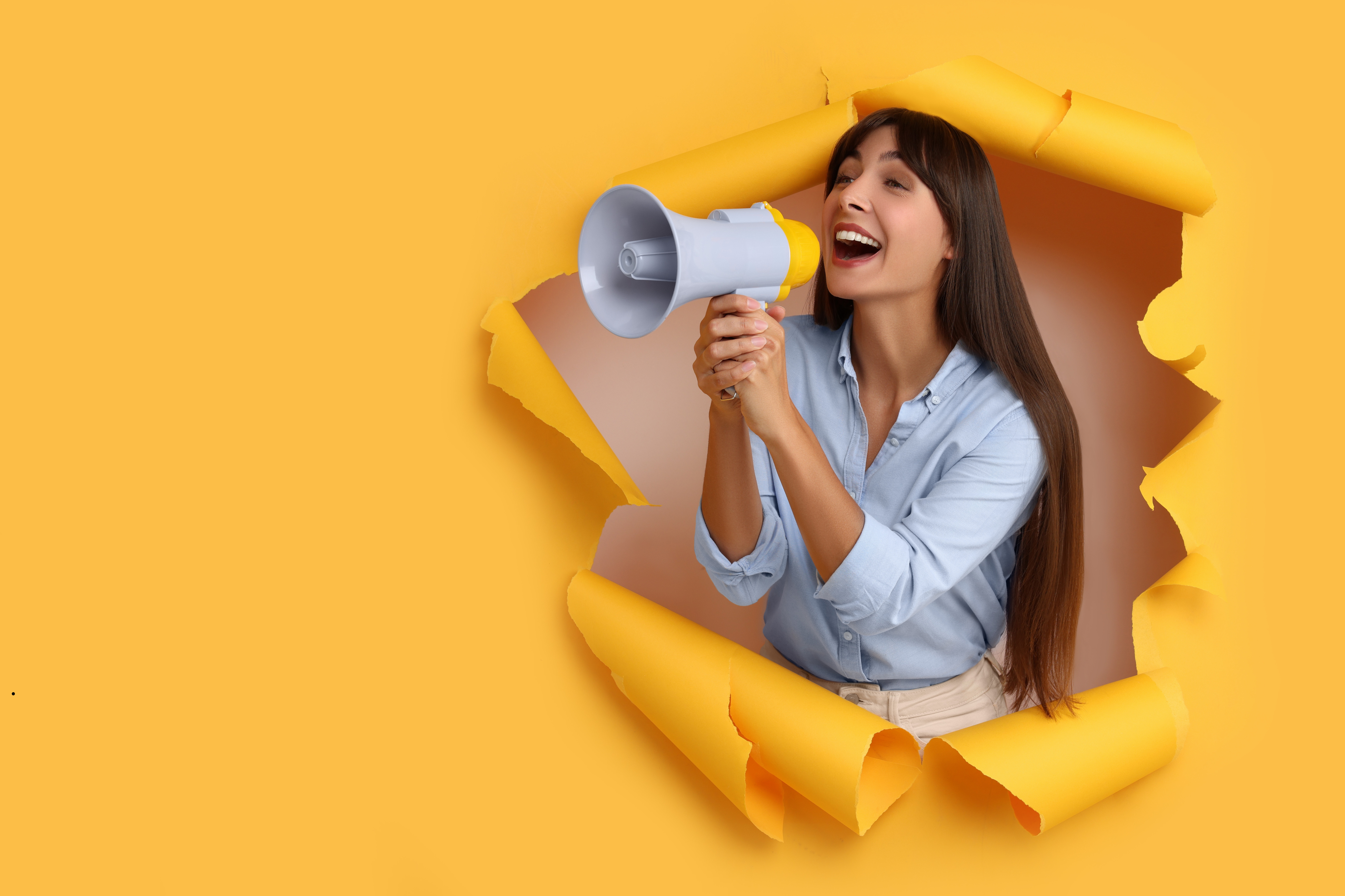 Zdjęcie przedstawia panią krzyczącą przez megafon, na żółtym tle1