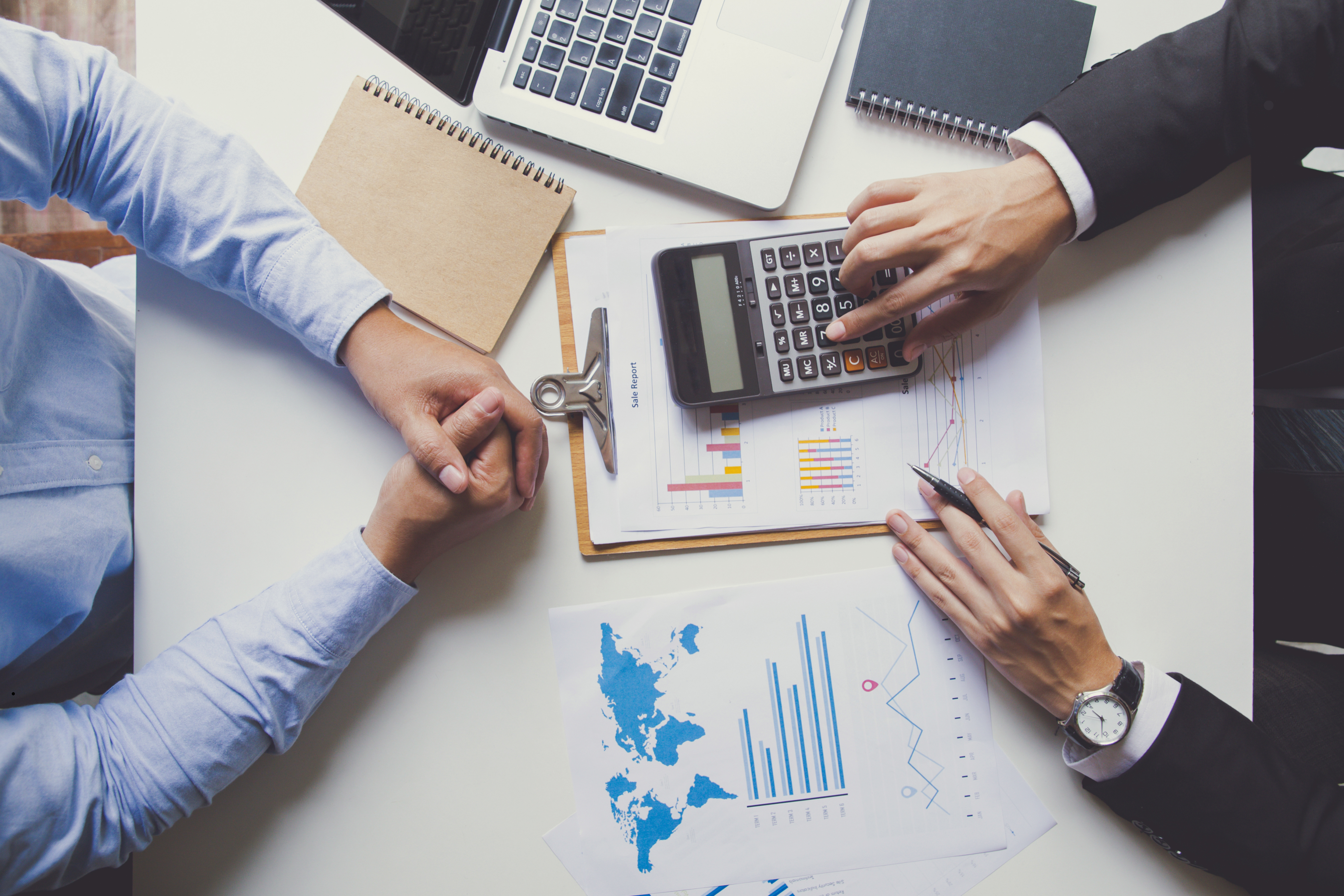 Zdjęcie przedstawia dwie osoby przy biurku z dokumentami i kalkulatorem.1