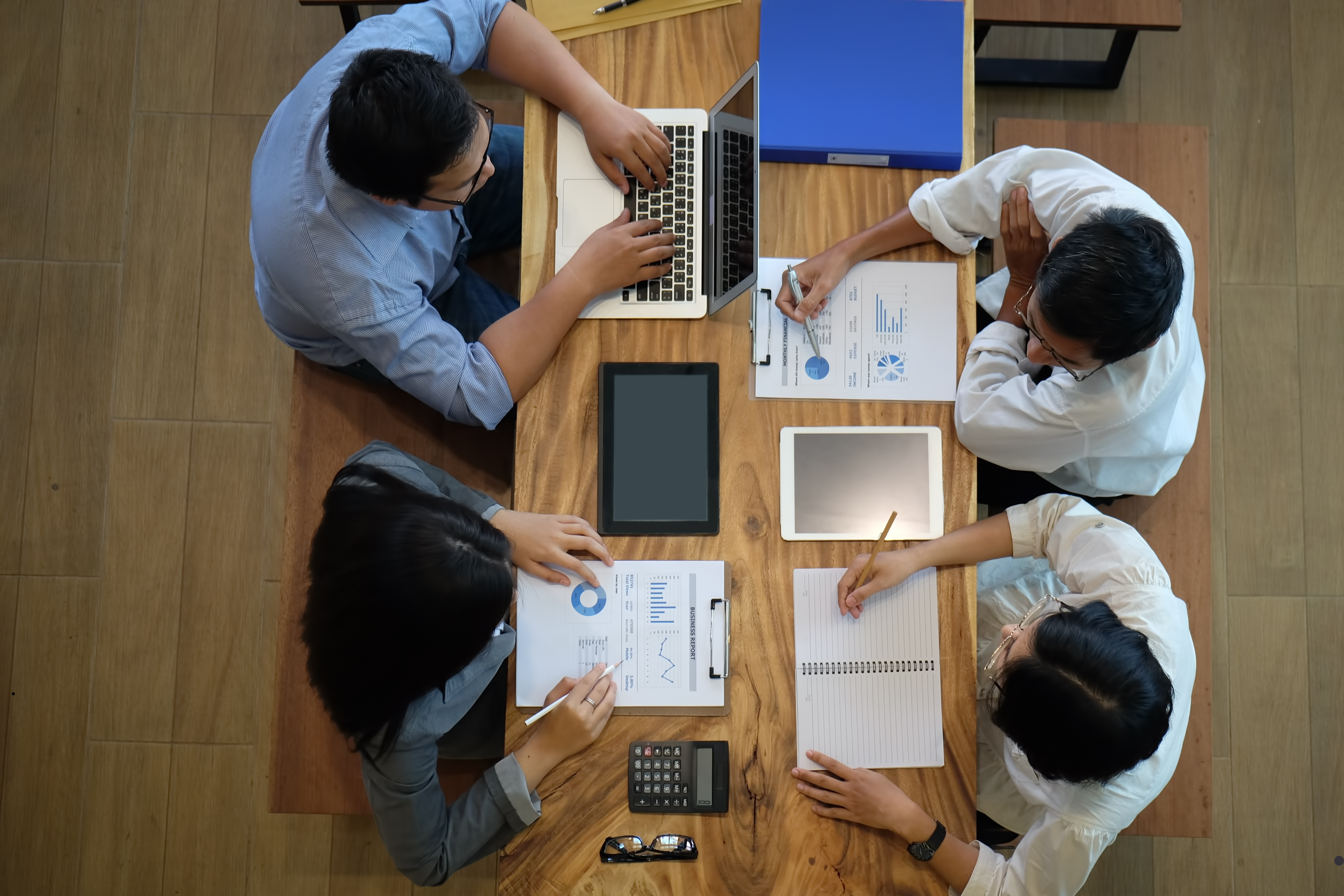 Zdjęcie przedstawia grupę osób siedzących przy stole, na którym leżą materiały biurowe.1